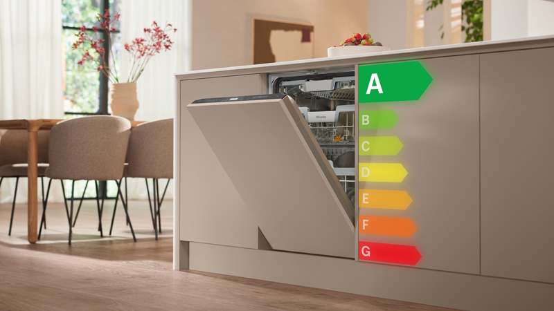 Miele Geschirrspüler in eleganter Küche, geöffnet mit sichtbarem Innenraum, daneben farbige Energieeffizienzskala mit grünem A – modernes, energiesparendes Gerät.
