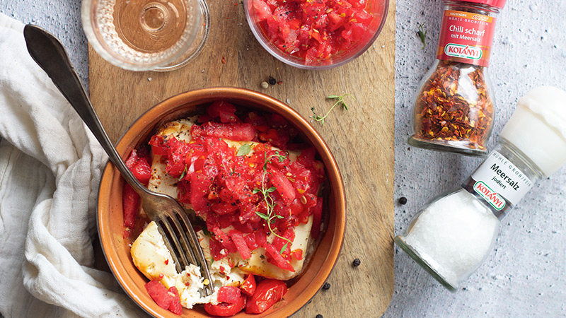 Abbildung: Banner mit Rezeptbild „Ofenfeta mit spicy Wassermelonen-Tomaten-Salsa“. Zu sehen sind eine Auflaufform mit gebackenem Feta und Tomaten-Wassermelonen-Salsa sowie Gewürze von Kotányi.